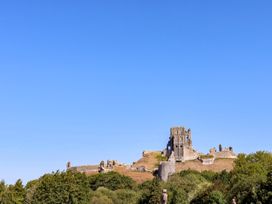 Castle ruins on a hill with trees in the foreground at Farthing Cottage Corfe Castle