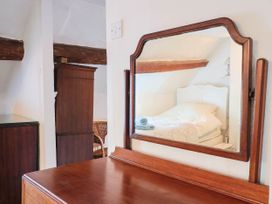 A mirror reflecting a bed and wooden furniture at Farthing Cottage in Corfe Castle