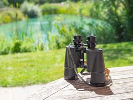 Binoculars on a wooden table near a lake at Ash Lodge in Stowmarket