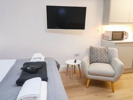 A bedroom with a television, armchair, and kitchenette at The Cabin in St Ives