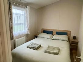 A bedroom with a double bed and nightstand at Surfside Bliss Cayton Bay Park caravan in Cayton Bay