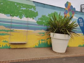 An outdoor area with a swing, wall mural and large planter at Golden Sands