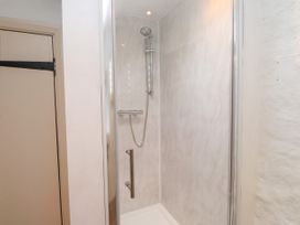 A shower with a glass door and showerhead at Felin Bach Aberdaron