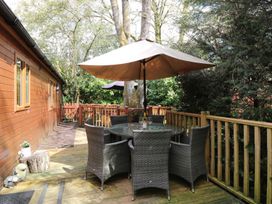 A table with chairs and a parasol on a deck at Fir Tree Lodge in Coniston 3, White Cross Bay near Windermere