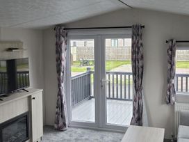 A living room with a television and door leading to a deck at 3 Bedroom Cabin Sleeps 6 - Shared Pool & Shared Hot Tub, Flamingo Land Resort near Malton