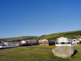 Mobile homes and a rock on grass with mountains in the background at Snowdonia Sunbeach Holiday Sea and Mountain view Llwyngwril