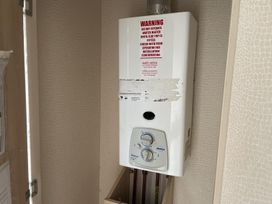 A water heater and warning notice in a utility room at 4 Bed Lodge Sleeps 8 - Pets & WiFi Free Parking in Ingoldmells