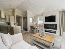 A living room with a sofa, dining area and wall-mounted television at 19 Pony Meadow near White Cross Bay