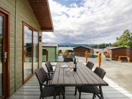 An outdoor dining area with a table and chairs overlooking a lake at 19 Pony Meadow White Cross Bay near Troutbeck Bridge