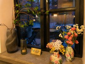 A window with vases of artificial flowers and a decorative sign at Muddy Boots – La Petite Mews in Kirby Stephen