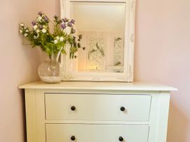 A drawer chest with a mirror and flowers at Muddy Boots – La Petite Mews in Kirby Stephen