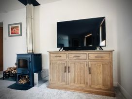 A living room with a television on a cabinet and a wood stove at Muddy Boots – Scarpa in Kirkby Stephen