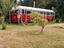 A red bus in a grassy area beside trees at Honey Bee Bus in Menheniot