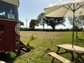An outdoor area with a red bus, table, and umbrella at Honey Bus in Menheniot