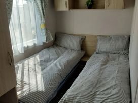 A bedroom with two single beds and a window at St Osyth Beach in St. Osyth