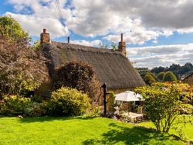 An outdoor area with a thatched roof cottage, garden furniture and plants