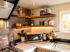 A kitchen with a stove, microwave, and shelves holding mugs and utensils at 