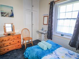 A bedroom with a bed, dresser, chair, mirror, and sink at Old Higher Lighthouse Stopes Cottage Portland Bill