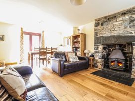 A living room with two leather sofas a wood-burning stove dining table and chairs a wooden bookshelf and wooden flooring at 3 Railway Cottages in Betws-y-Coed