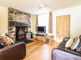A living room with a stone fireplace two leather sofas a wooden floor and a television at 3 Railway Cottages Betws-y-Coed
