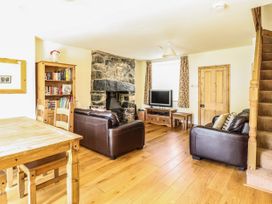 A living room with a stone fireplace brown leather sofas wooden dining table bookshelf television and carpeted stairs at 3 Railway Cottages in Betws-y-Coed