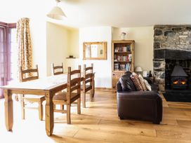 A dining area with wooden table and chairs next to a living space with leather sofa and stone fireplace at 3 Railway Cottages in Betws-y-Coed