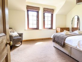 A bedroom with a bed a striped armchair two windows and a wooden dresser with a mirror at 3 Railway Cottages in Betws-y-Coed