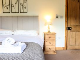 A bedroom with a bed with white sheets and pillows a bedside table with a lamp wooden door and artwork on the wall at 3 Railway Cottages in Betws-y-Coed