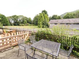 An outdoor seating area with metal table and chairs next to a wooden fence overlooking railway tracks and a building surrounded by trees at 3 Railway Cottages in Betws-y-Coed