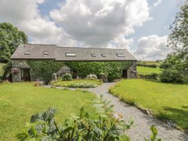 A stone house with ivy on the walls and a gravel path leading to the entrance surrounded by grass and flowers at Arfron Penrhyddion Pella in Capel Garmon near Betws-y-Coed