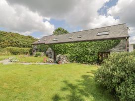 A stone house covered with ivy with roof windows and a grassy lawn with flower pots at Arfron Penrhyddion Pella in Capel Garmon near Betws-y-Coed