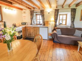 A kitchen and living area with wooden ceiling beams a round dining table with flowers a sofa and windows with curtains at Arfron Penrhyddion Pella in Capel Garmon near Betws-y-Coed