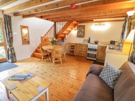 A living area with wooden floor and beams kitchen with stove dining table with chairs sofa and coffee table at Arfron Penrhyddion Pella in Capel Garmon near Betws-y-Coed