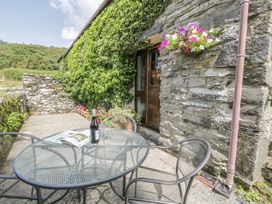 An outdoor patio with a metal table and chairs a bottle of wine and an open magazine on the table stone walls with hanging flowers and plants at Arfron Penrhyddion Pella in Capel Garmon near Betws-y-Coed