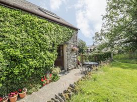 An exterior view of a stone house with ivy on the walls a pathway with flower pots a round table with chairs and a grassy garden at Arfron Penrhyddion Pella in Capel Garmon near Betws-y-Coed