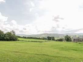 A green field with trees a stone house and hills in the background at Arfron Penrhyddion Pella in Capel Garmon near Betws-y-Coed