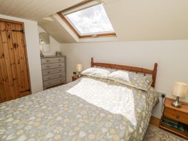 A bedroom with a wooden bed frame a patterned duvet two bedside tables with lamps a chest of drawers and a skylight window at Meifod Penrhyddion Pella in Capel Garmon near Betws-y-Coed