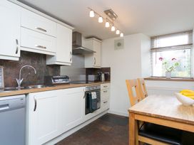 A kitchen with white cabinets wooden countertop a dining table and chairs and a window with blinds and a plant at Harrisons Cottage in Llandegla near Llangollen