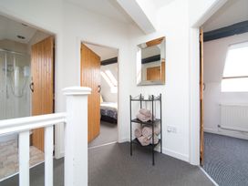 A hallway with three wooden doors one leading to a bathroom with a shower one to a bedroom and one to another room with a window a small black metal shelf with rolled towels and a rectangular wall mirror at Harrisons Cottage in Llandegla near Llangollen