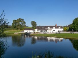 A pond in front of a white building with picnic tables and trees at Harrisons Cottage in Llandegla near Llangollen