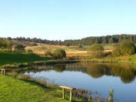 A pond with benches and a picnic table near grass and trees at Harrisons Cottage in Llandegla near Llangollen
