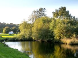 A pond with trees and grassy banks and a white caravan in the background at Harrisons Cottage in Llandegla near Llangollen