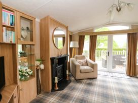 A living room with a beige armchair and fireplace next to glass doors and windows at The Four Oaks Chalet in Blaich near Fort William