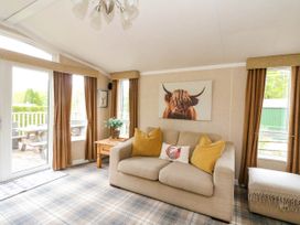 A living room with a beige sofa and yellow cushions a wooden side table and windows with brown curtains at The Four Oaks Chalet in Blaich near Fort William