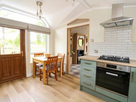 A kitchen with a wooden dining table and four chairs next to a glass door and window with a stove and oven on the right at The Four Oaks Chalet in Blaich near Fort William