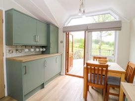 A dining area with wooden table and chairs next to green kitchen cabinets and an open door to a deck at The Four Oaks Chalet in Blaich near Fort William