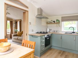 A kitchen with green cabinets a gas stove a kettle and a window next to a dining table and a living room at The Four Oaks Chalet in Blaich near Fort William