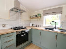 A kitchen with green lower cabinets wooden countertops a black oven a gas stove a sink under a window and a shelf with plants at The Four Oaks Chalet in Blaich near Fort William