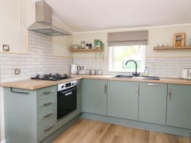 A kitchen with green cabinets wooden countertops a gas stove an oven a black sink under a window and kitchen shelves at The Four Oaks Chalet in Blaich near Fort William