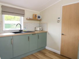 A kitchen with green cabinets a black sink a toaster a clock and a wooden door at The Four Oaks Chalet in Blaich near Fort William